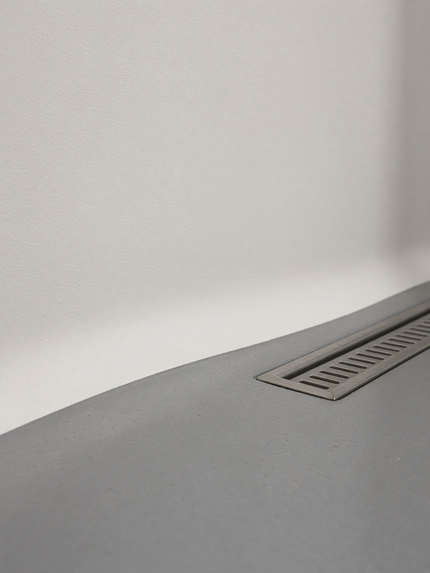 Resin coving where a grey floor curves up into a plain wall, with a stainless drain
